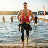 Man in a colorful swimsuit walking out of the water on a beach with other participants in the background.