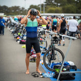 Athlete in triathlon gear preparing for a race with bicycles and equipment around.